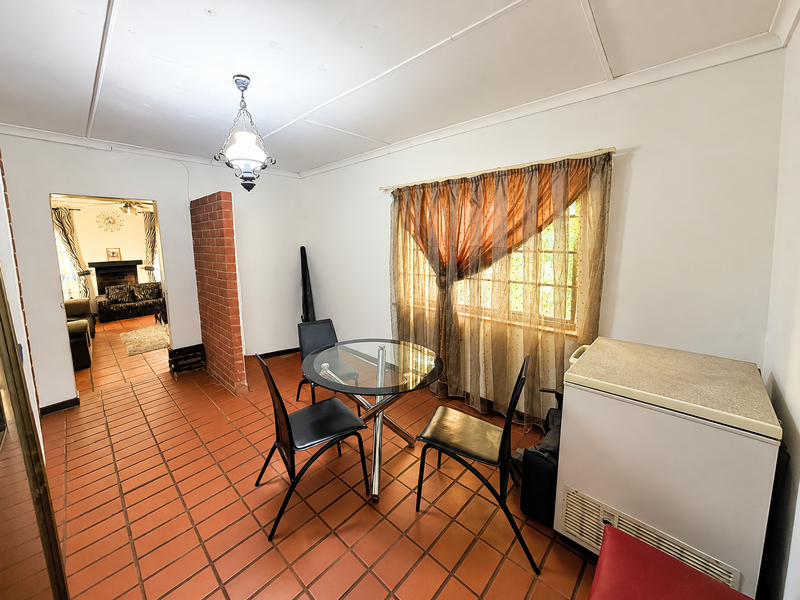Dining area featuring terracotta floor tiles, an exposed brick partition wall, and a view into the adjacent living room.