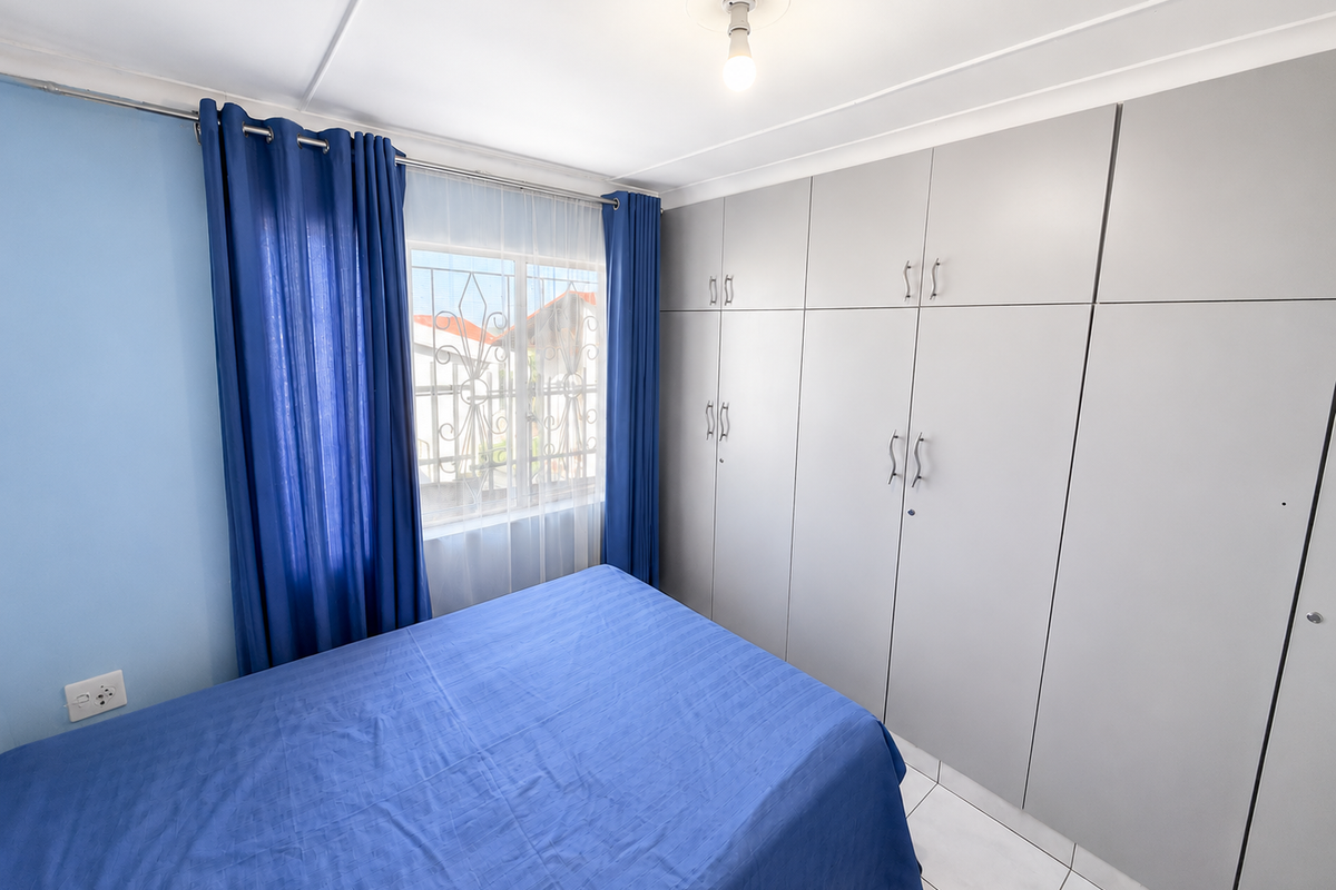 A bright bedroom featuring built-in floor-to-ceiling cabinetry, tiled flooring, and a window with security bars.