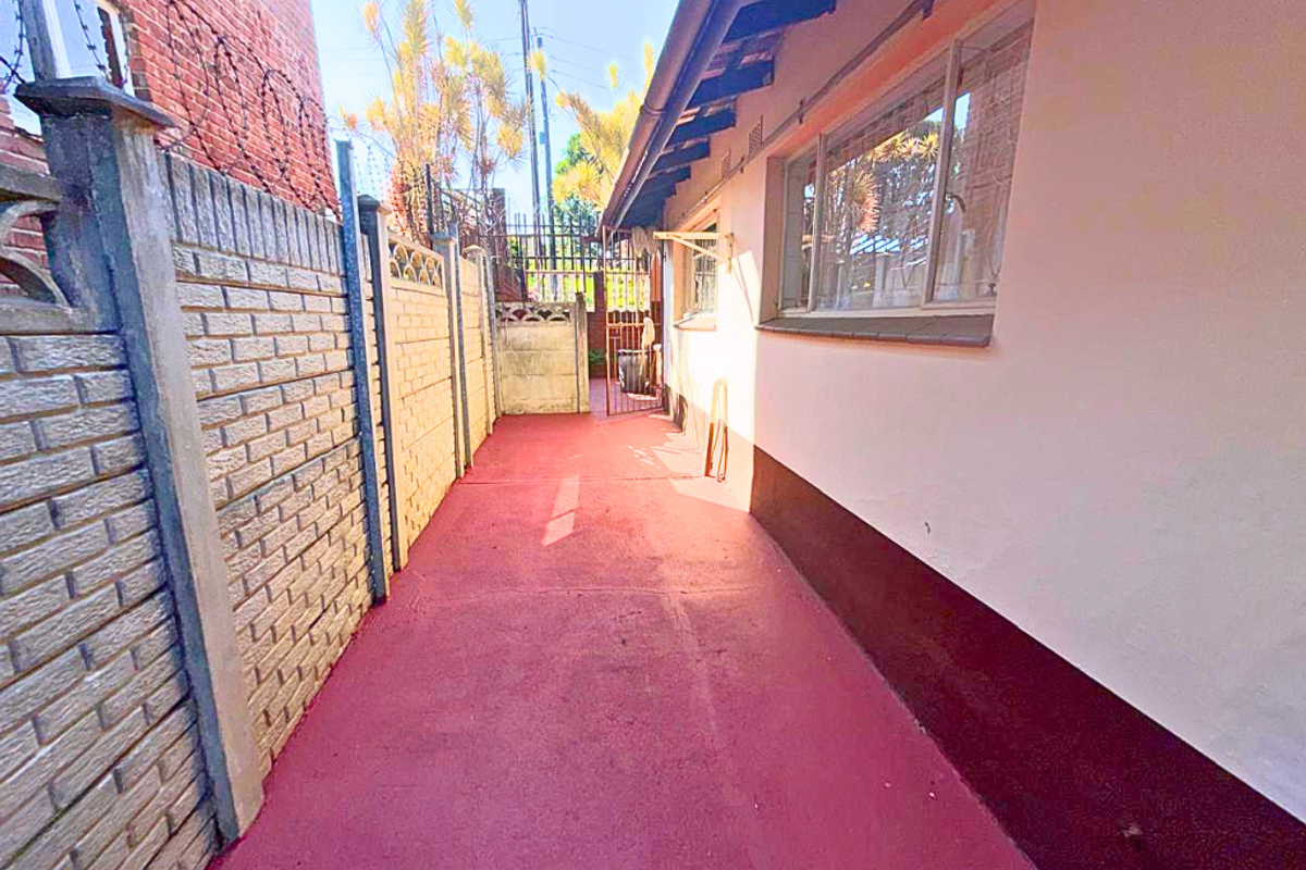 A side exterior walkway featuring a painted concrete path, enclosed by a brick boundary wall and the side elevation of the house.