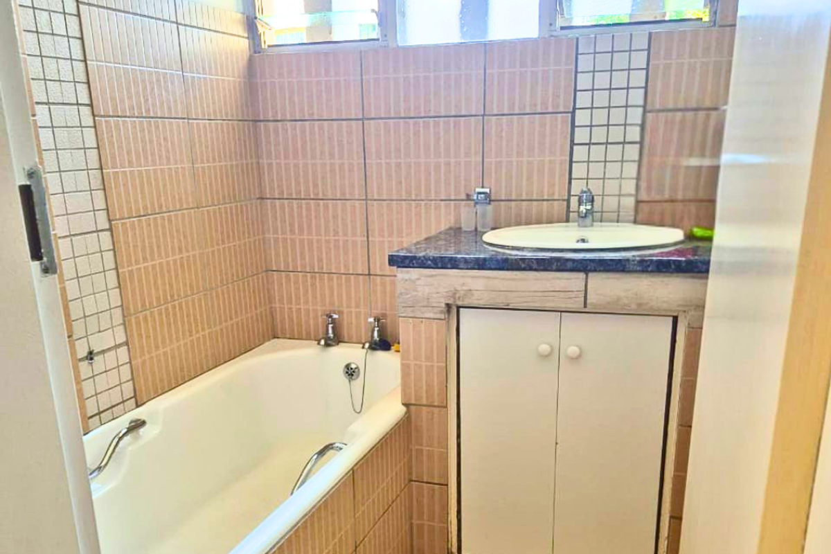 A functional bathroom featuring a built-in bathtub, a vanity cabinet with a countertop basin, and tiled wall finishes.