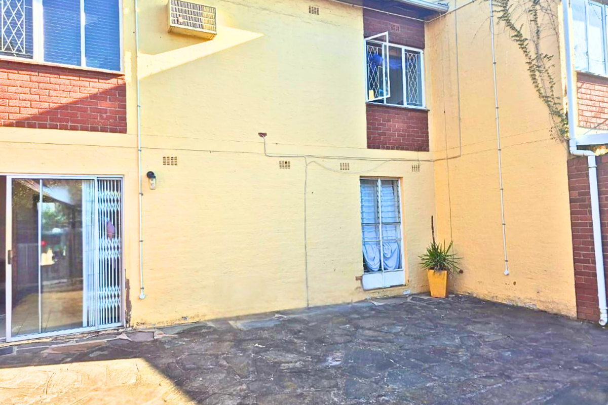 Rear exterior view of the townhouse featuring a paved patio area, brick and rendered facade, and sliding glass door access.