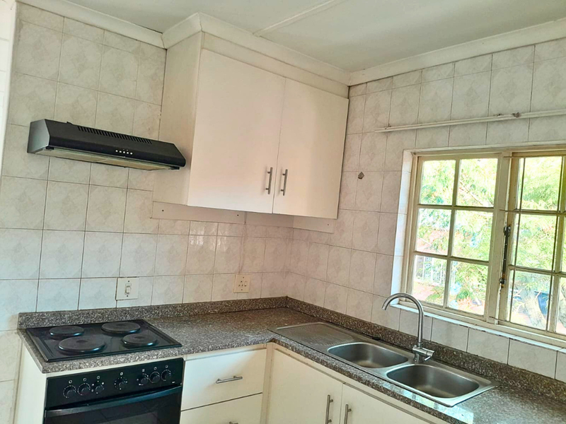 A functional kitchen featuring built-in cabinetry, an electric stove with extractor fan, a double basin sink, and tiled backsplash with a window view.