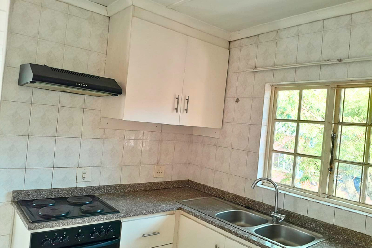 A functional kitchen featuring built-in cabinetry, an electric stove with extractor fan, a double basin sink, and tiled backsplash with a window view.