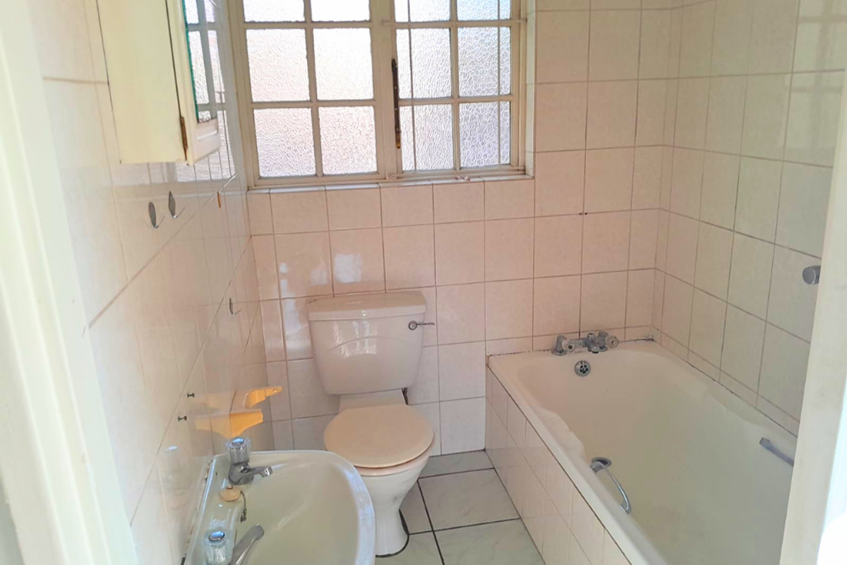 A dated bathroom featuring a built-in bathtub, pedestal washbasin, toilet, and full-height ceramic wall tiling with an obscure glass window.