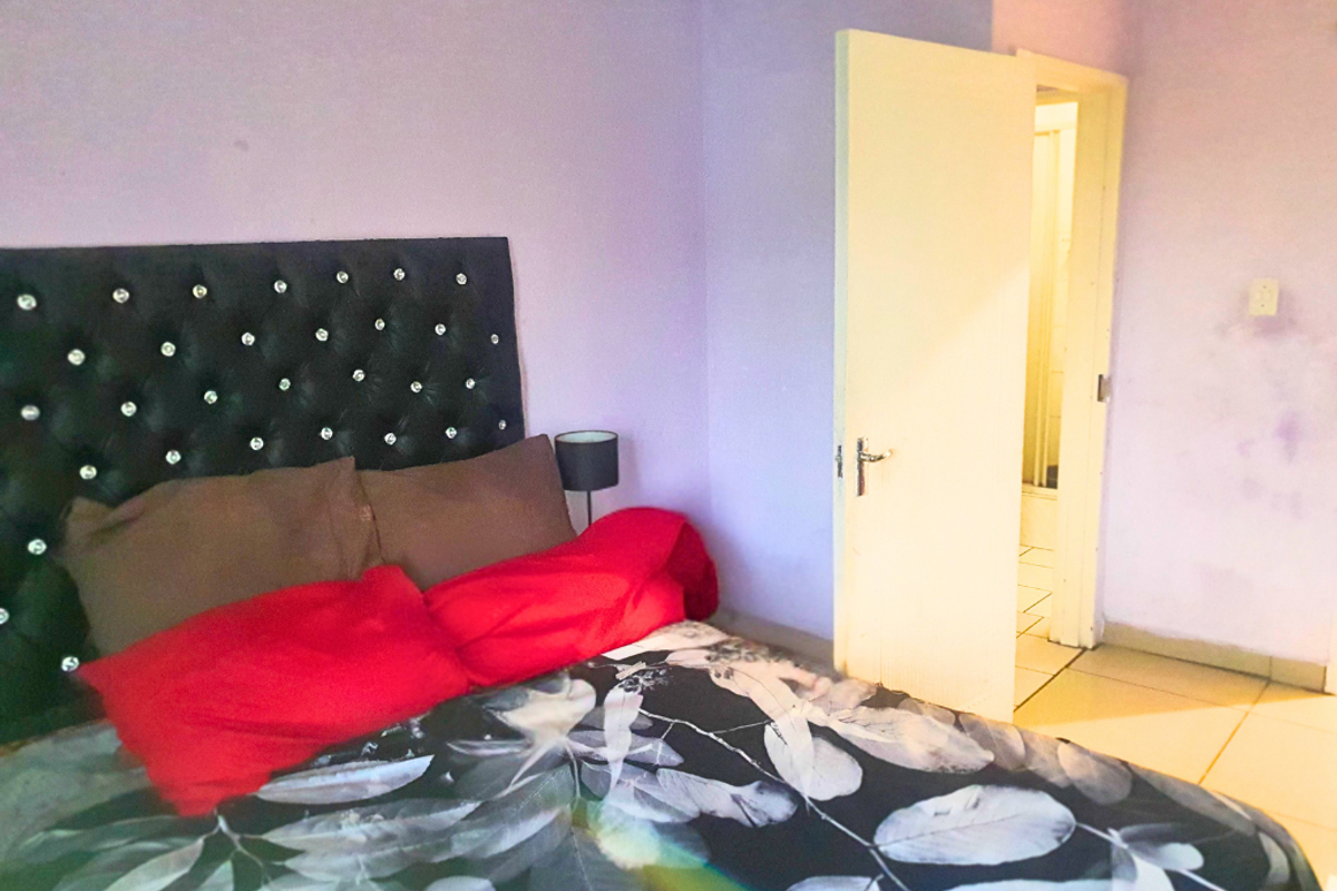 A bedroom featuring light purple walls and an adjacent doorway leading to an en-suite bathroom with tiled flooring.