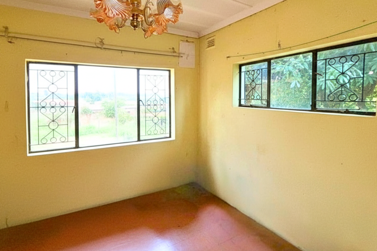 A vacant bedroom featuring large windows with security bars, a vintage chandelier, and original flooring, offering a blank canvas for renovation.
