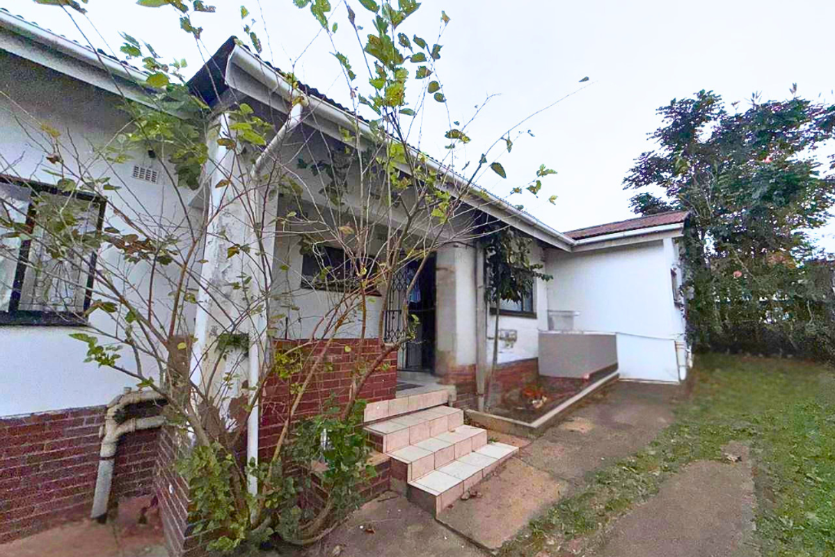 Rear exterior view of the house featuring a covered entrance, tiled steps, and brick facade elements with visible signs of weathering.