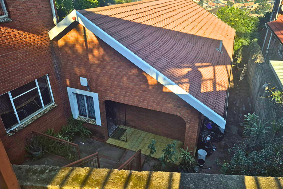 An elevated view of the rear exterior featuring a brick facade, tiled roof, and a covered patio area with access steps.