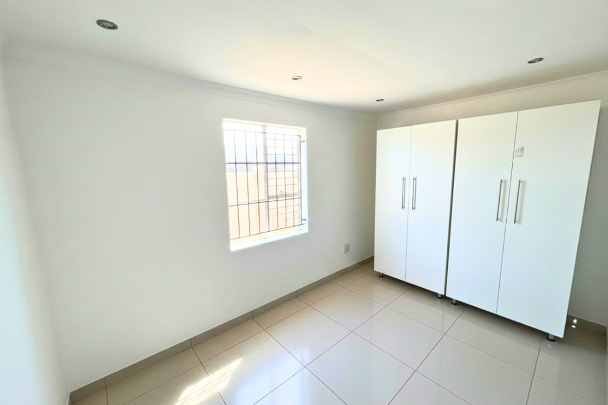 A bright, empty bedroom featuring neutral tiled flooring, recessed downlighting, and white built-in cupboards with modern hardware.