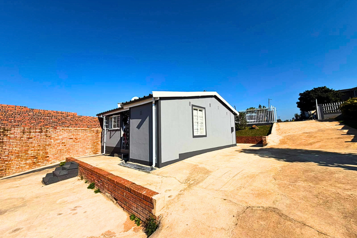 Rear view of the property featuring a concrete driveway, brick boundary wall, and secure access points with security bars.