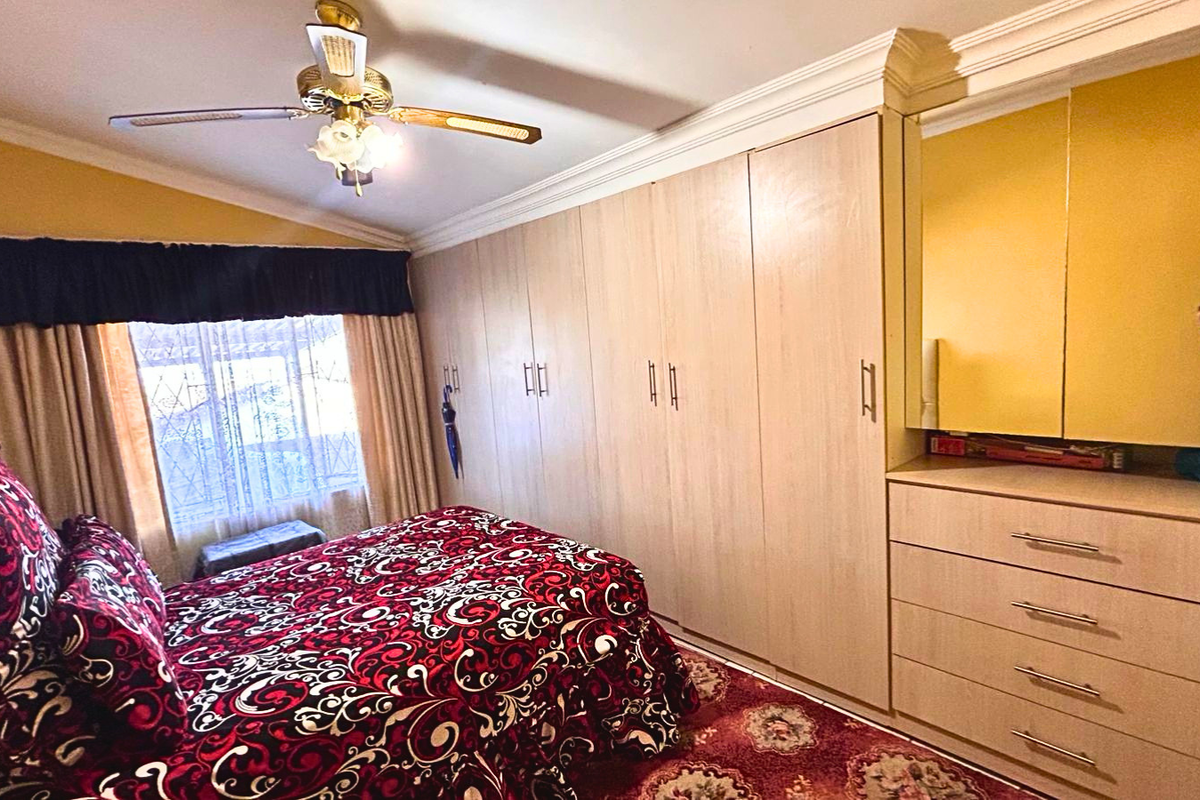 A bedroom featuring extensive built-in cabinetry with integrated drawers and a vanity mirror, complemented by a ceiling fan and crown molding.