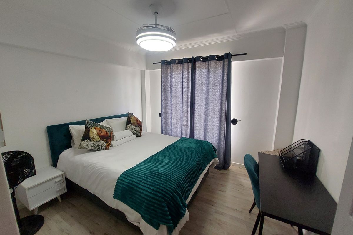 A well-maintained bedroom featuring light-toned laminate flooring, a modern ceiling fan, and floor-to-ceiling curtains.
