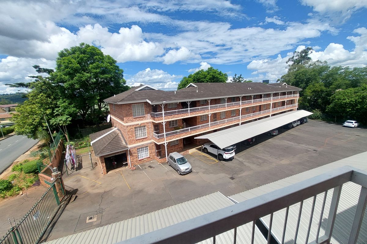 An elevated view of a multi-story brick townhouse complex featuring covered parking bays, balconies, and secure perimeter fencing.