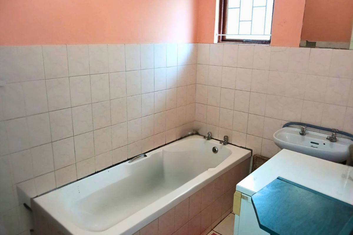 A dated bathroom featuring a built-in bathtub, wall-mounted basin, and tiled splashbacks, requiring cosmetic updates to modernize the space.