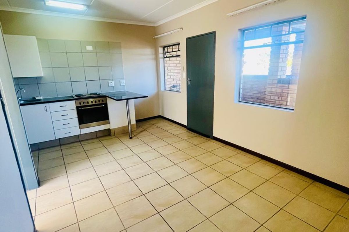 A functional, empty kitchen featuring tiled flooring, built-in cabinetry, a built-in oven, and a hob, providing a clean canvas for potential updates.