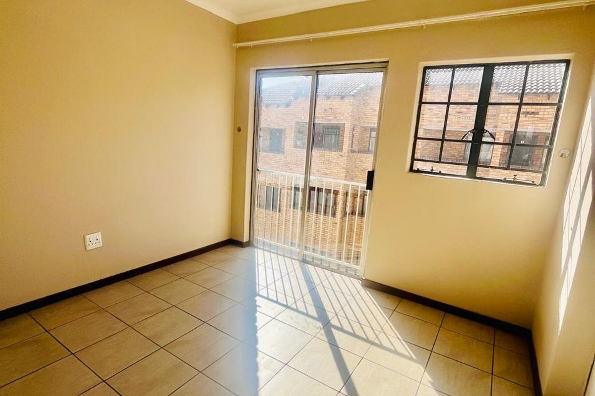 A bright, empty bedroom featuring tiled flooring, a sliding glass door leading to a balcony, and a window with security bars.