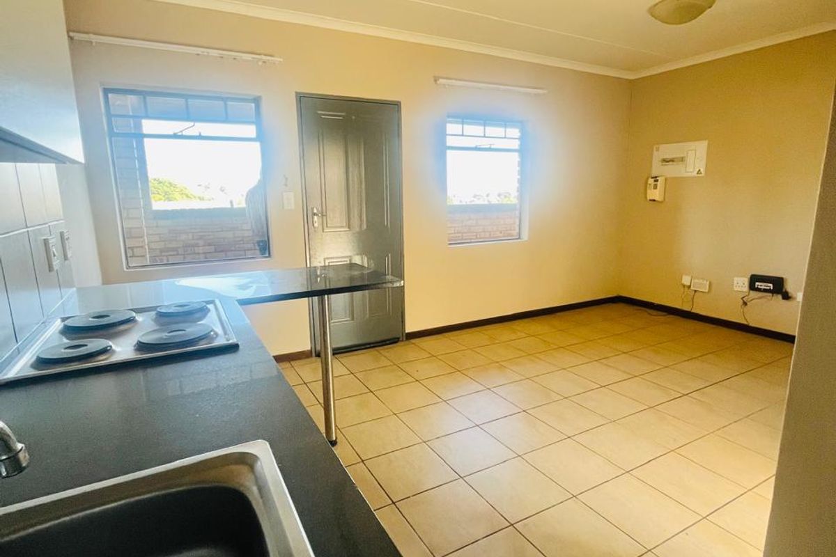 An open-plan kitchen and living area featuring tiled flooring, a built-in electric hob, and a functional breakfast bar in a neutral setting.