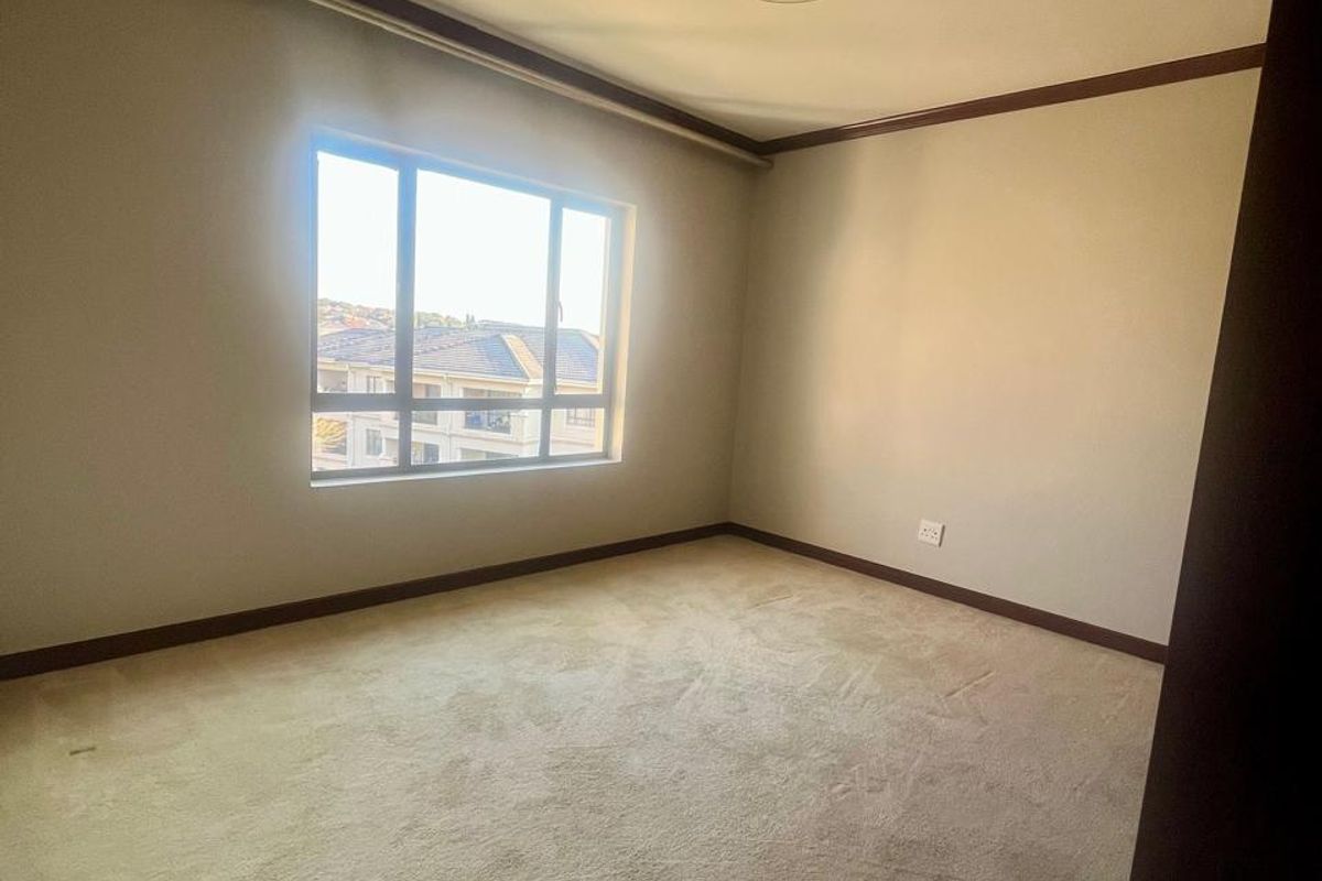 A spacious, empty bedroom featuring neutral carpeting, a ceiling light fixture, and a large window providing natural light.
