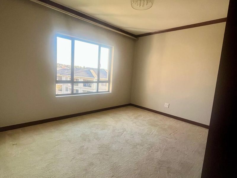 A spacious, empty bedroom featuring neutral carpeting, a ceiling light fixture, and a large window providing natural light.