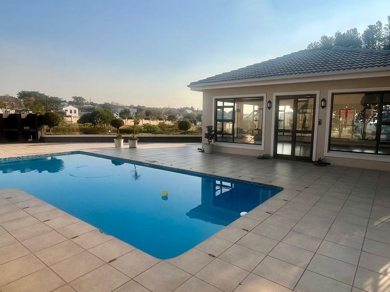 A well-maintained outdoor pool area featuring a tiled deck, clear swimming pool, and direct access to the main building structure.