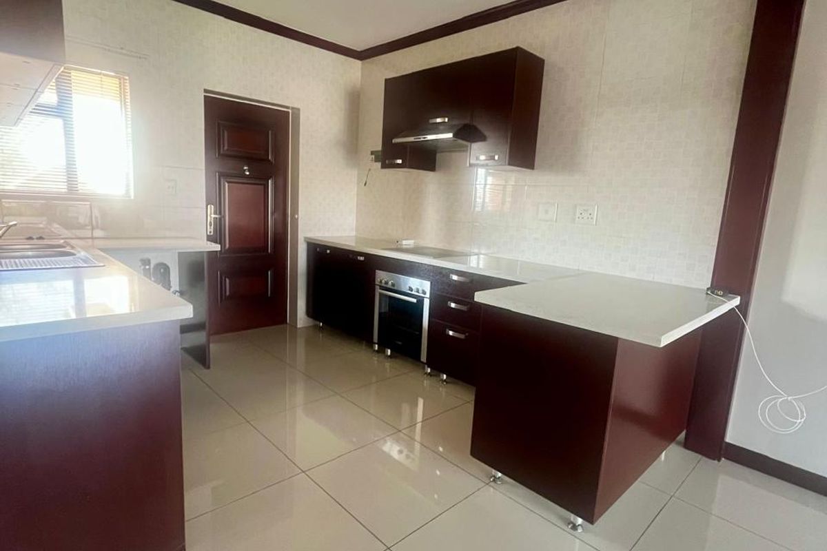 A clean, modern kitchen featuring dark wood cabinetry, white stone countertops, built-in oven, extractor fan, and polished ceramic floor tiles.