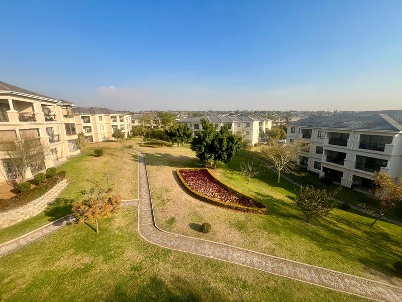 An elevated aerial view of the apartment complex grounds, featuring well-maintained lawns, landscaped garden beds, and paved walkways between residential buildings.