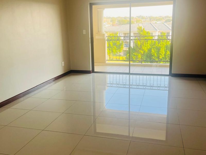 A bright, empty living room featuring polished tiled flooring and a large sliding glass door that opens onto a balcony with neighborhood views.