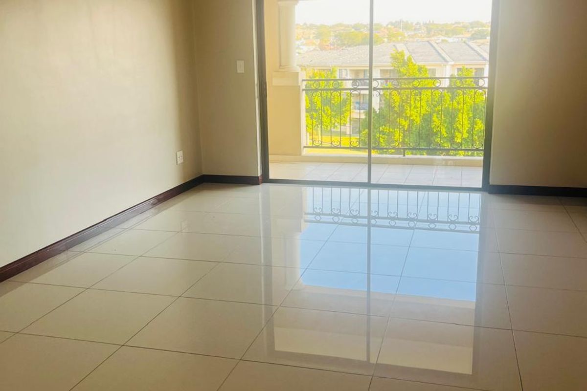 A bright, empty living room featuring polished tiled flooring and a large sliding glass door that opens onto a balcony with neighborhood views.