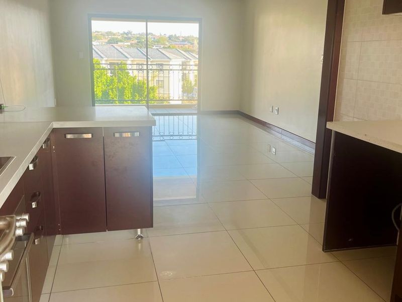 An open-plan kitchen and living area featuring tiled flooring, built-in cabinetry, and a sliding glass door leading to a balcony with neighborhood views.