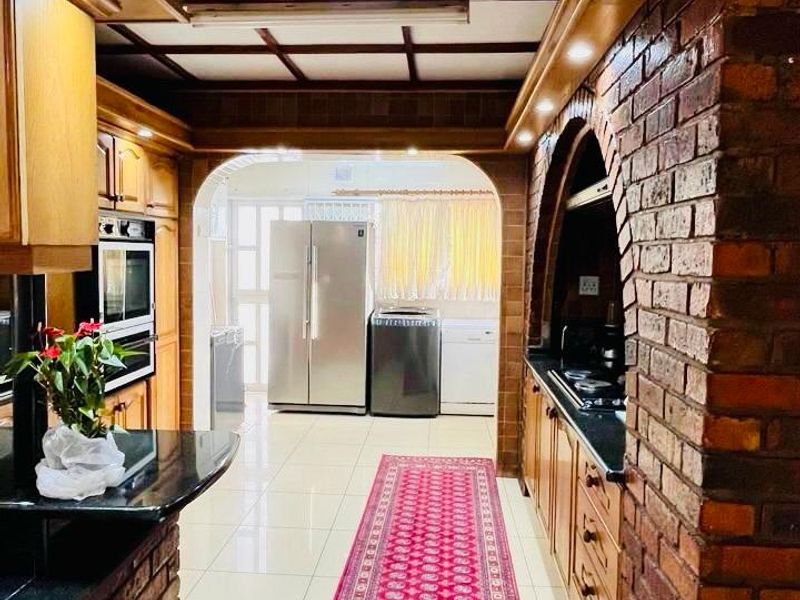 A rustic-style kitchen featuring exposed brick arches, timber ceiling beams, granite countertops, and built-in cabinetry with a connected laundry area.