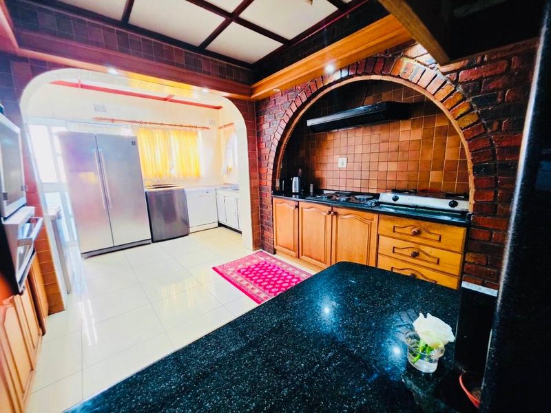 Spacious kitchen featuring a distinctive brick archway, timber cabinetry, granite countertops, and a gas hob, offering a rustic yet functional cooking space.