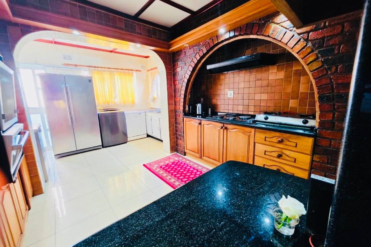 Spacious kitchen featuring a distinctive brick archway, timber cabinetry, granite countertops, and a gas hob, offering a rustic yet functional cooking space.
