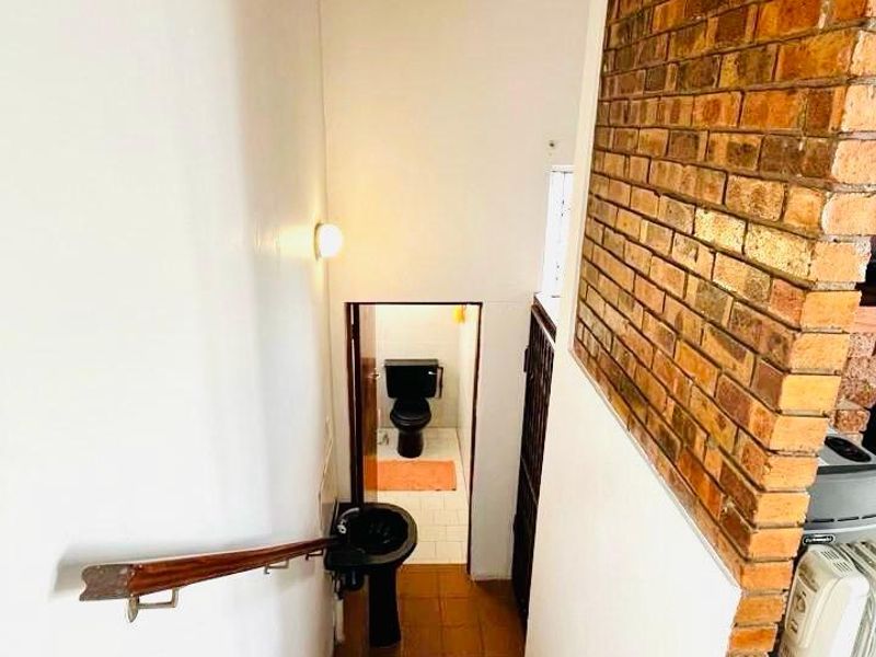 A staircase with tiled steps and an exposed brick feature wall leading down to a small bathroom area with a pedestal basin and toilet.