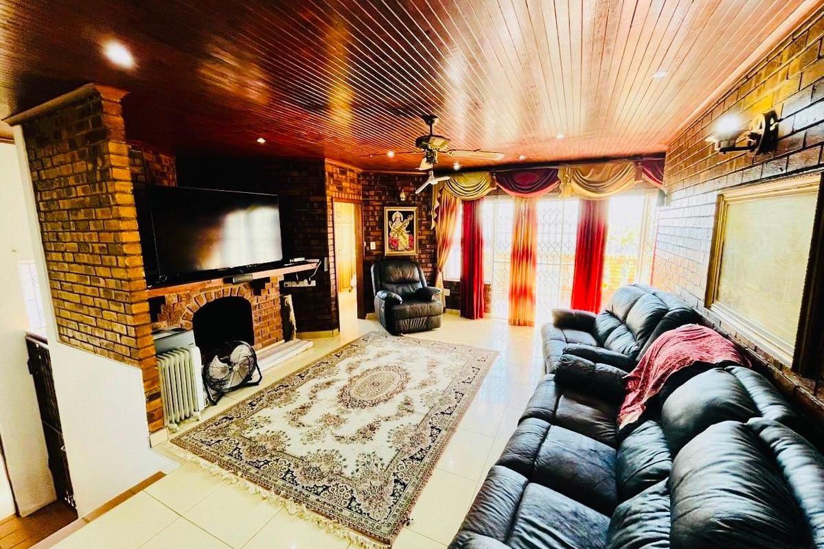 Spacious living room featuring exposed brick walls, a warm timber ceiling, tiled floors, and a built-in brick fireplace with access to outdoor space.