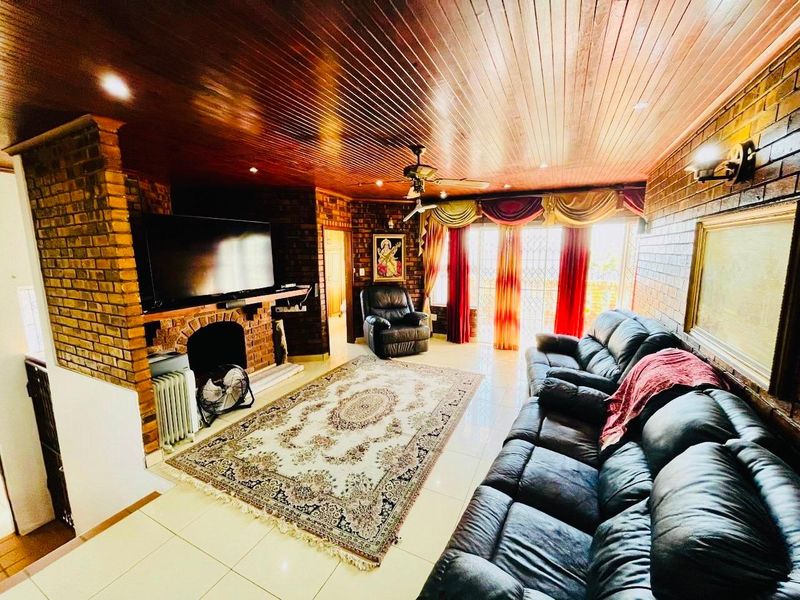 Spacious living room featuring exposed brick walls, a warm timber ceiling, tiled floors, and a built-in brick fireplace with access to outdoor space.