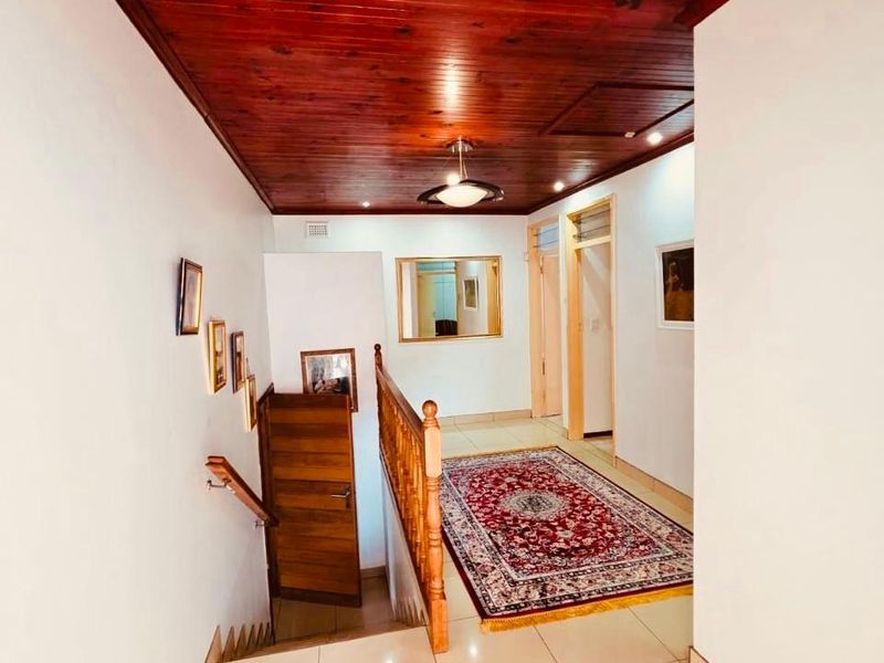 A bright hallway featuring tiled flooring and a distinctive dark timber tongue and groove ceiling, leading to a wooden staircase with a matching balustrade.