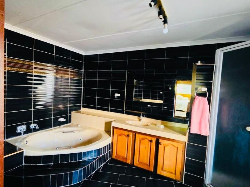 A spacious bathroom featuring a built-in corner bathtub, vanity cabinet with integrated basin, and a separate shower enclosure with dark tiled finishes.