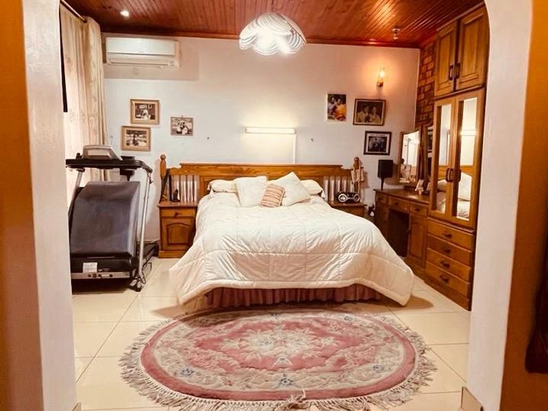 Spacious bedroom featuring a warm timber ceiling, tiled flooring, built-in cabinetry, and a split-system air conditioner, accessed via a raised brick step.