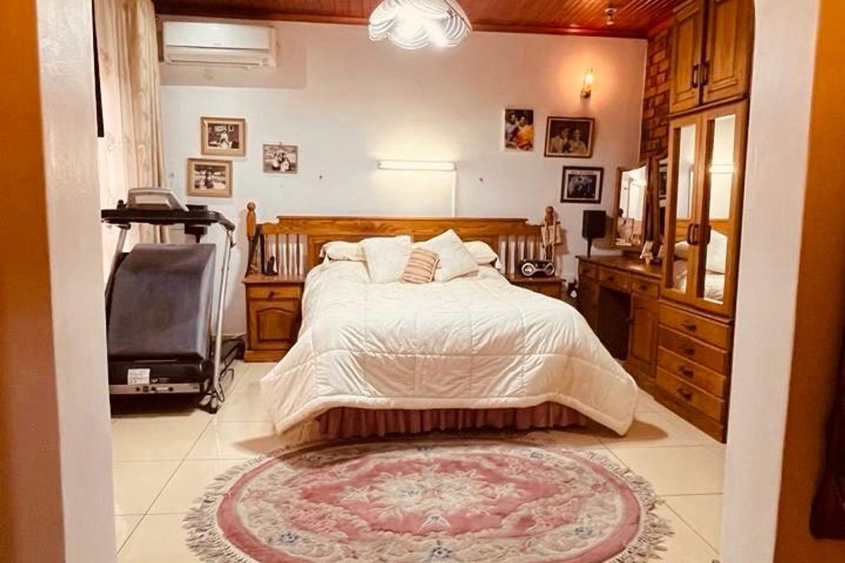 Spacious bedroom featuring a warm timber ceiling, tiled flooring, built-in cabinetry, and a split-system air conditioner, accessed via a raised brick step.