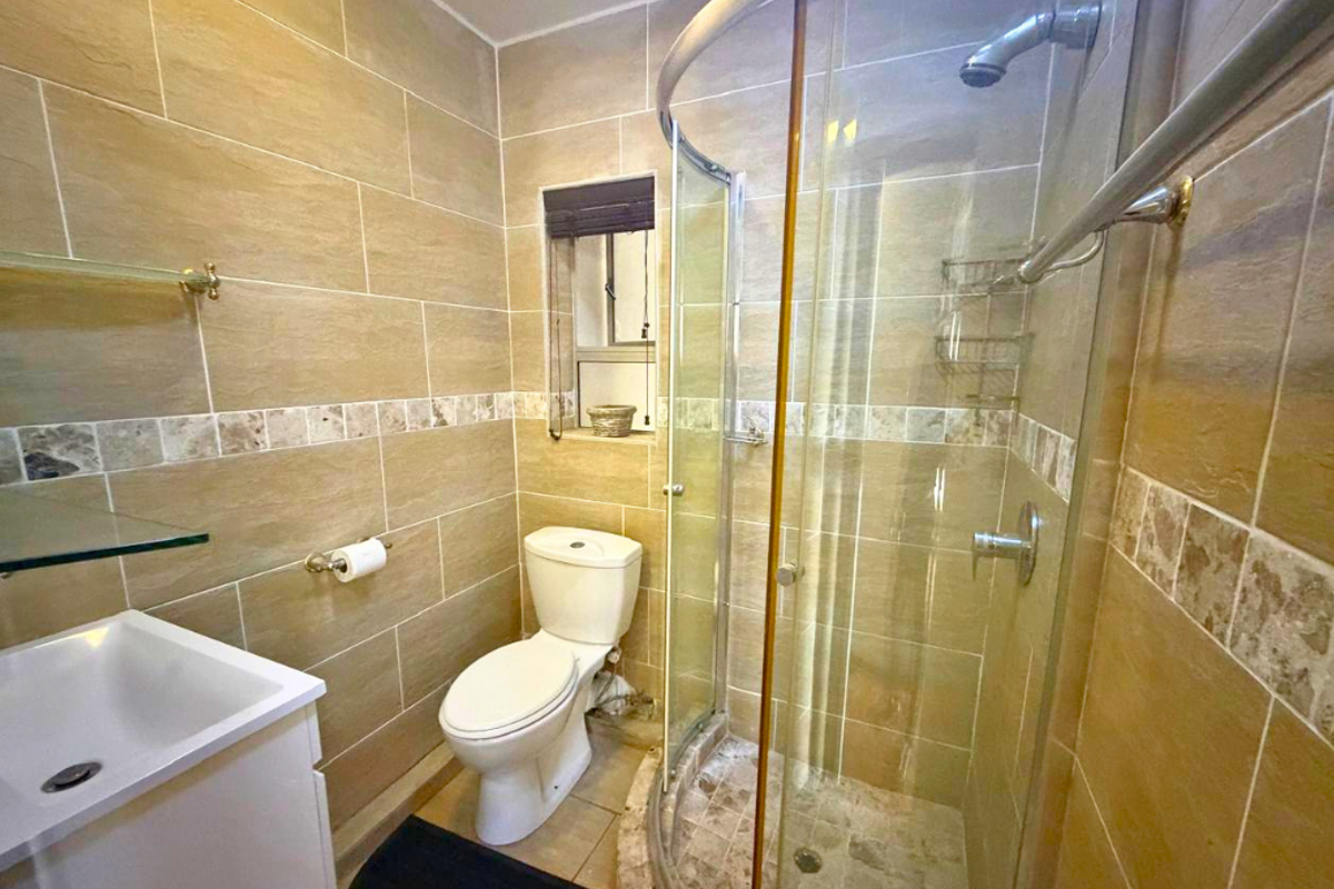 A compact, modern bathroom featuring a curved glass shower enclosure, tiled walls with a decorative border, a vanity basin, and a standard toilet.