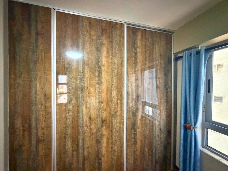 A bedroom featuring a large built-in sliding door wardrobe with a wood-grain finish and an aluminium-framed window.