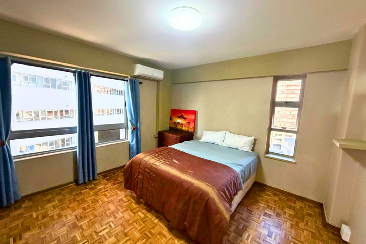 A bedroom featuring classic parquet flooring, a wall-mounted air conditioning unit, and large windows providing natural light.