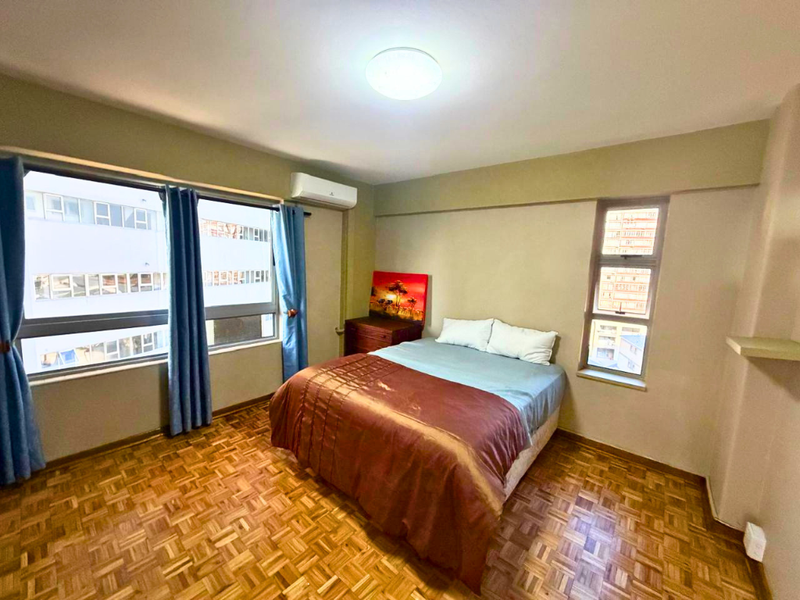 A bedroom featuring classic parquet flooring, a wall-mounted air conditioning unit, and large windows providing natural light.