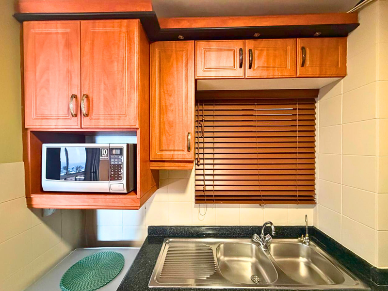 A functional kitchen area featuring dark granite countertops, a double bowl stainless steel sink, and warm-toned built-in cabinetry with integrated microwave space.