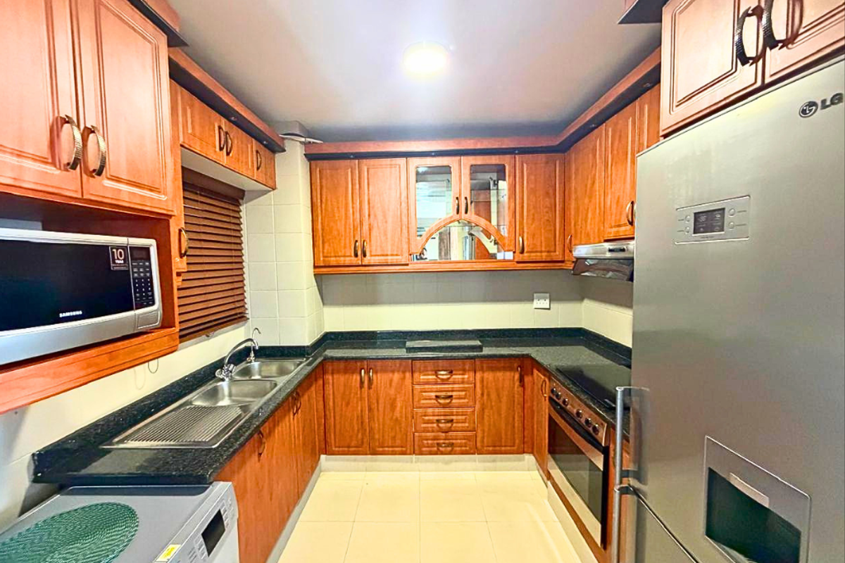A functional U-shaped kitchen featuring warm-toned laminate cabinetry, granite countertops, integrated appliances, and tiled flooring, offering ample storage and workspace.