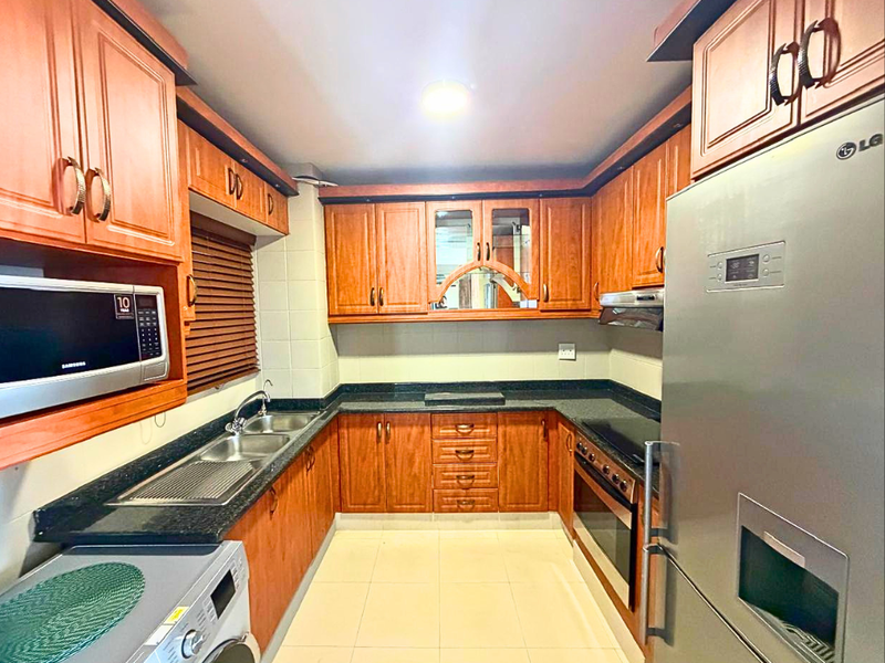 A functional U-shaped kitchen featuring warm-toned laminate cabinetry, granite countertops, integrated appliances, and tiled flooring, offering ample storage and workspace.