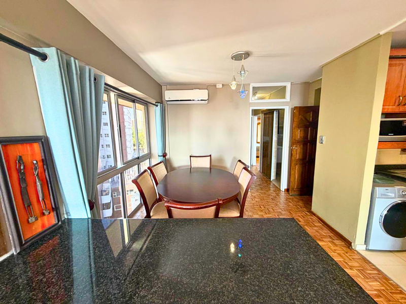 Open plan living and dining area featuring parquet flooring, granite kitchen countertops, and a wall-mounted air conditioning unit.