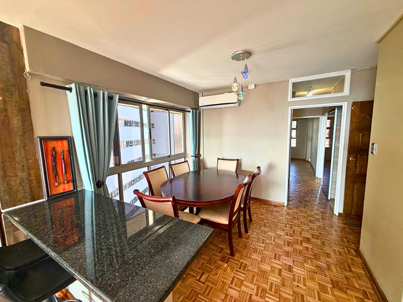Open-plan dining area featuring parquet flooring, a granite breakfast counter, and a wall-mounted air conditioning unit, leading into a hallway.