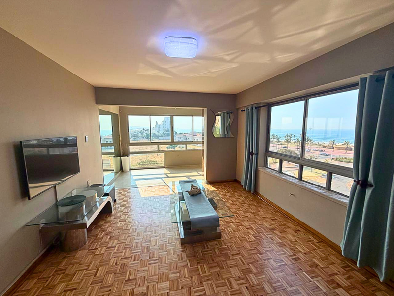 Spacious living area featuring classic parquet flooring, large windows with ocean views, and an integrated balcony space.