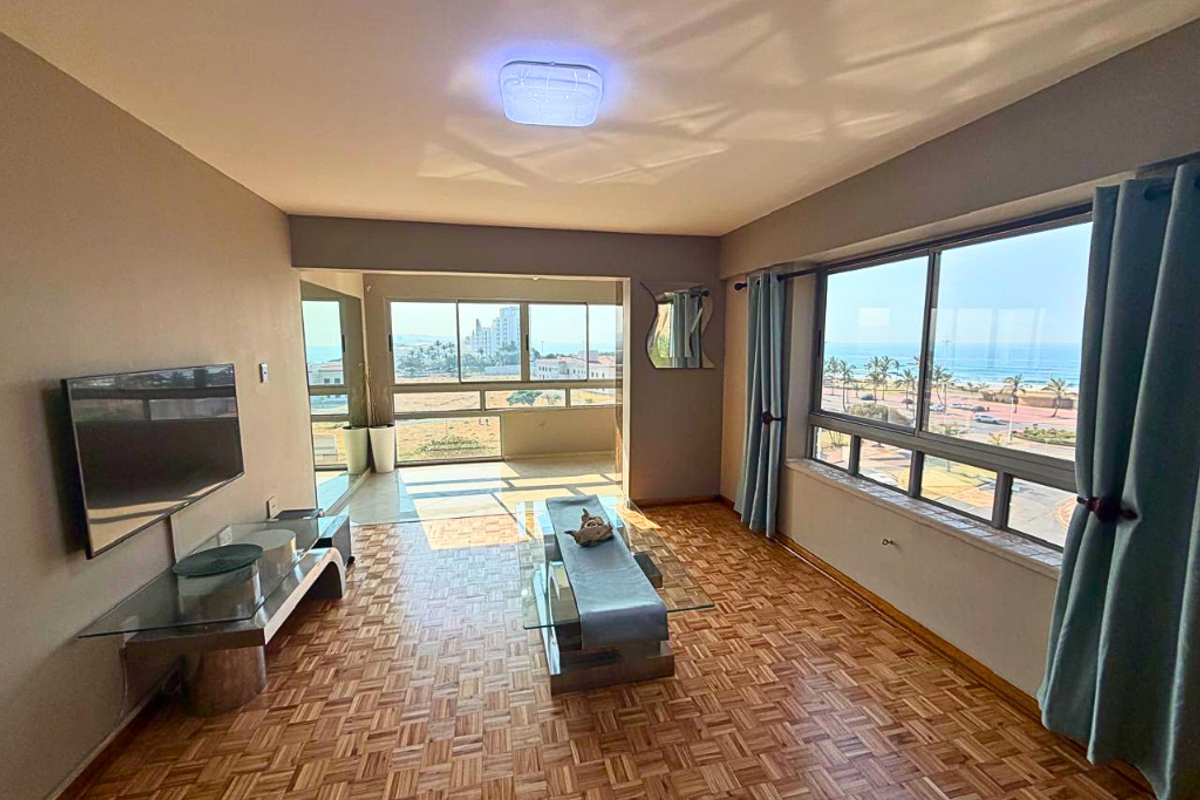 Spacious living area featuring classic parquet flooring, large windows with ocean views, and an integrated balcony space.